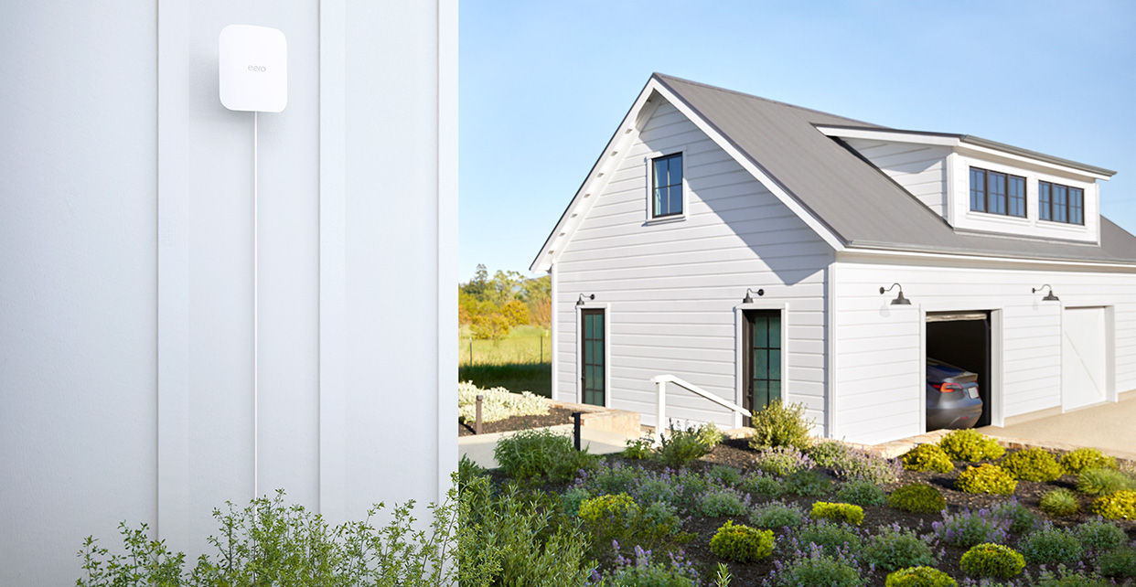eero Outdoor 7 mounted on an exterior wall with an outbuilding beyond it